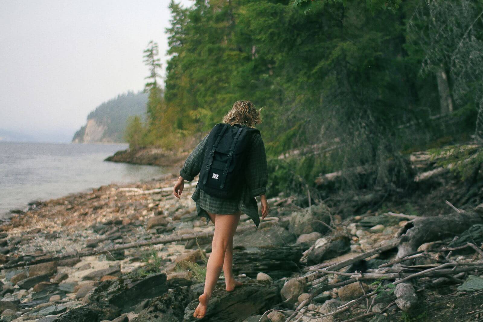 woman is walking barefoot near lake shore